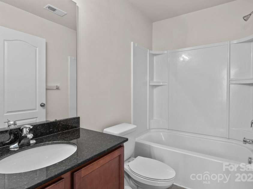 12550 McGrath Drive, Charlotte, NC 28269.  MLS# CAR4242569, YatesRealty ID 11597. This secondary en-suite bath boasts a sleek vanity with a granite countertop, clean lines, and a bright, inviting atmosphere.