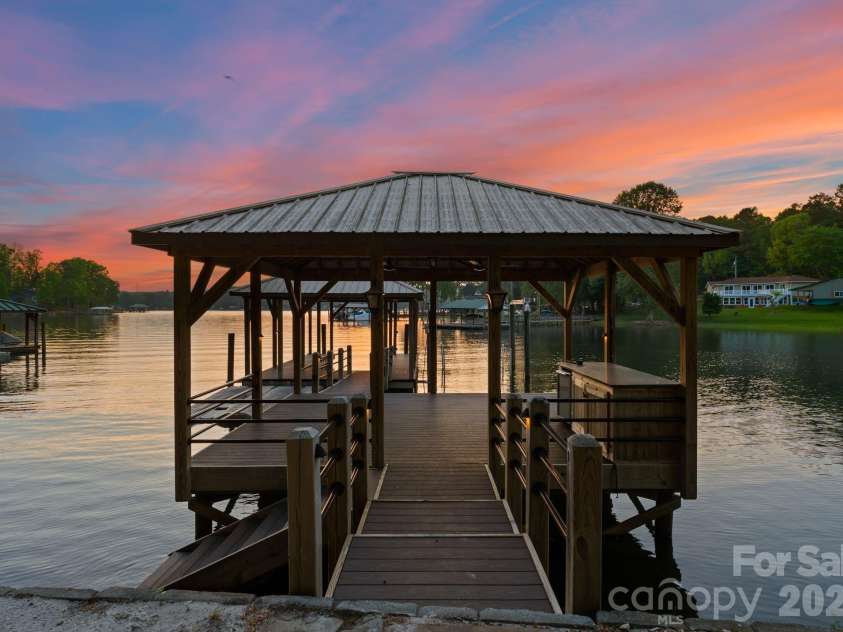 172 Tennessee Circle, Mooresville, NC 28117.  MLS# CAR4252701, YatesRealty ID 1230. The private dock features covered boat storage, two jet ski ports, an island with built-in storage and mini-fridge, ceiling fans, and a sand-lined lounging area along the water’s edge.