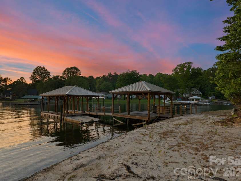 172 Tennessee Circle, Mooresville, NC 28117.  MLS# CAR4252701, YatesRealty ID 1230. The private dock features covered boat storage, two jet ski ports, an island with built-in storage and mini-fridge, ceiling fans, and a sand-lined lounging area along the water’s edge.