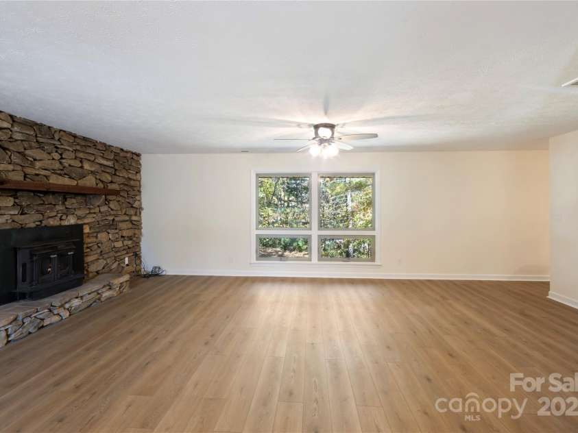 90 Joe Jenkins Road, Fairview, NC 28730.  MLS# CAR4288516, YatesRealty ID 12466. Spacious living room with a stone wall and a wood-burning stove, perfect for creating a cozy atmosphere.