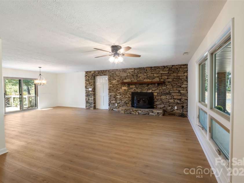 90 Joe Jenkins Road, Fairview, NC 28730.  MLS# CAR4288516, YatesRealty ID 12466. Spacious living room with a stone wall and a wood-burning stove, perfect for creating a cozy atmosphere.