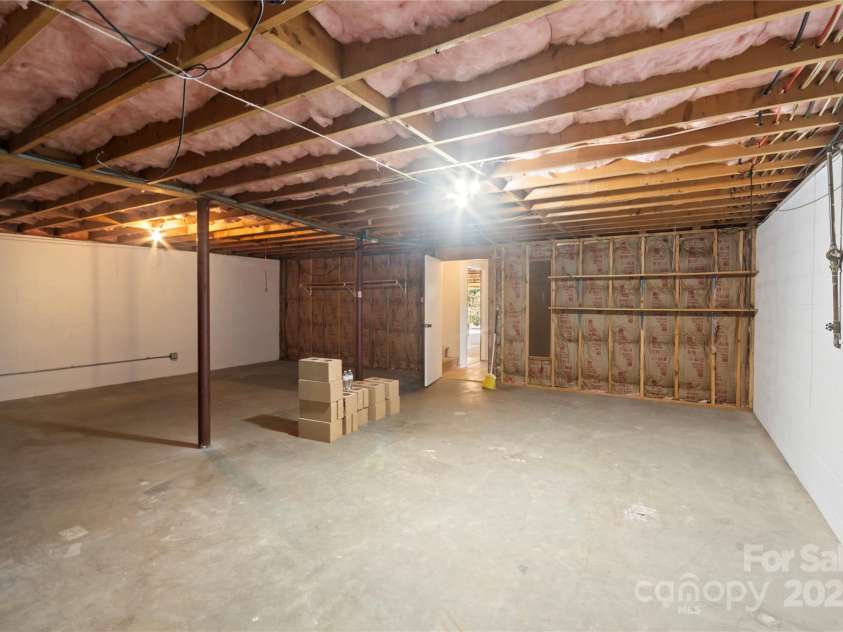 90 Joe Jenkins Road, Fairview, NC 28730.  MLS# CAR4288516, YatesRealty ID 12466. This basement features a generously sized room, offering immense potential to be transformed into a space perfectly tailored to your individual tastes and needs. The room boasts a rustic and inviting stone wall, complem