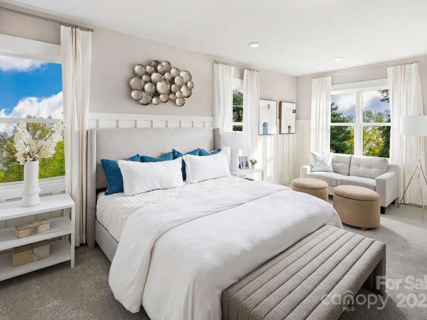 9408 Munsing Drive, Charlotte, NC 28269.  MLS# CAR4235913, YatesRealty ID 12701. *This image is not of the actual home, but a photo of our model home, shown for representative purposes.* Spacious primary suite with abundant natural light and a cozy seating area, perfect for relaxation.