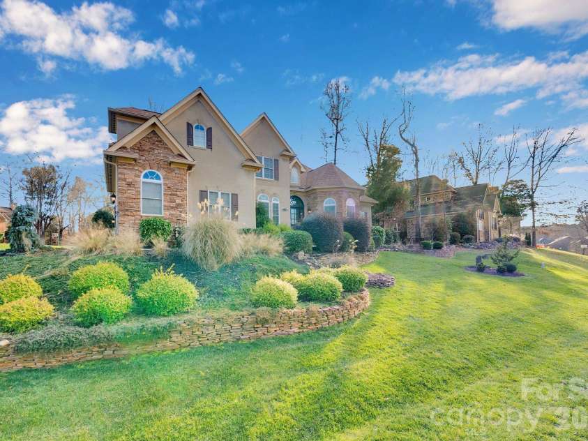 7778 Burning Ridge Drive, Stanley, NC 28164.  MLS# CAR4336313, YatesRealty ID 13726. Attractive front elevation showcasing a blend of stone and stucco, arched windows, and a welcoming entry. Thoughtfully landscaped grounds and a spacious lawn enhance curb appeal.
