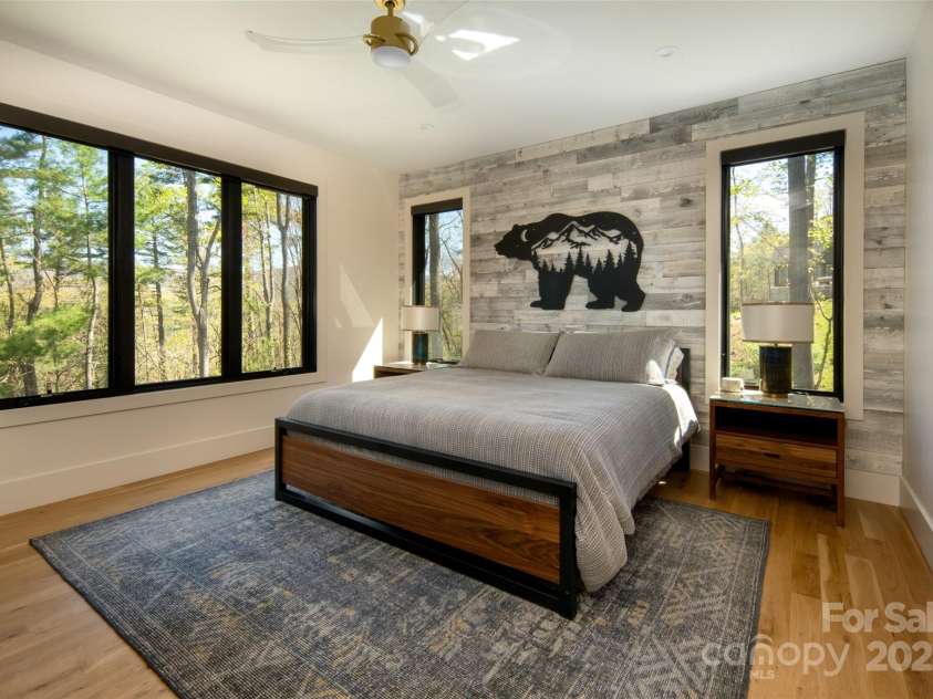 42 Spring Cove Road, Asheville, NC 28804.  MLS# CAR4246585, YatesRealty ID 13759. First of two large primary ensuite bedrooms with tons of natural light, gorgeous hardwood floors, wood accent wall, stunning views and remote-controlled motorized Smith & Noble solar shades (motorized shades in ALL bed