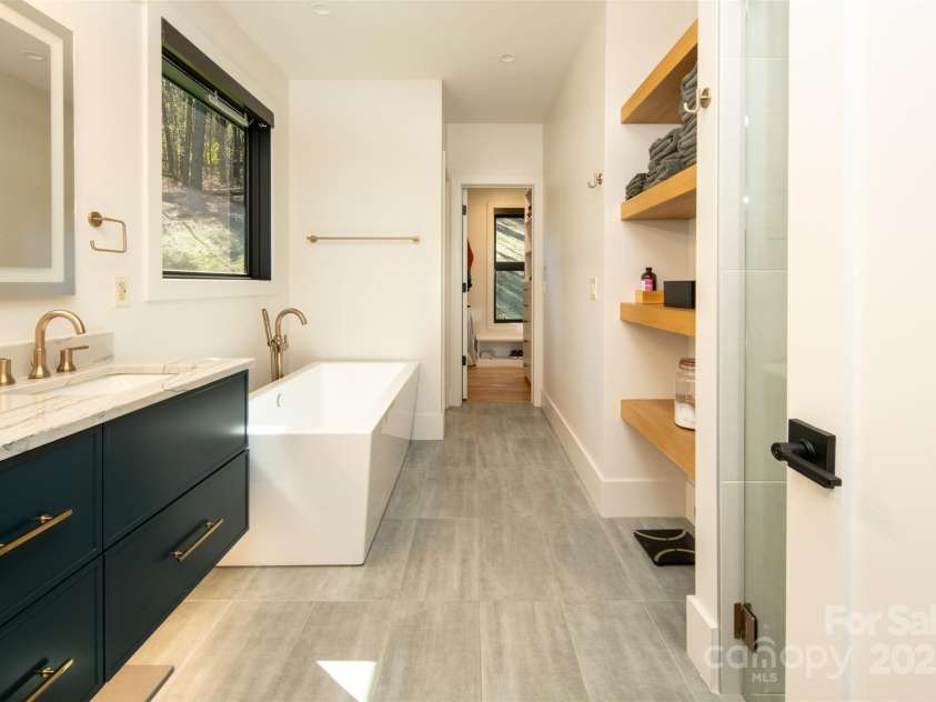 42 Spring Cove Road, Asheville, NC 28804.  MLS# CAR4246585, YatesRealty ID 13759. Primary ensuite bath with soaking tub, separate stand-up shower, floating double vanity with LED-lighted vanity mirror.  Bath leads to massive walk-in/wrap-around closet and adjoining laundry with washer/dryer and more