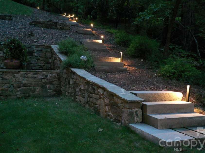 559 Shining Rock Path, Horse Shoe, NC 28742.  MLS# CAR4372540, YatesRealty ID 14910. Terraced stone landscaping with illuminated pathway steps leading into the forest.