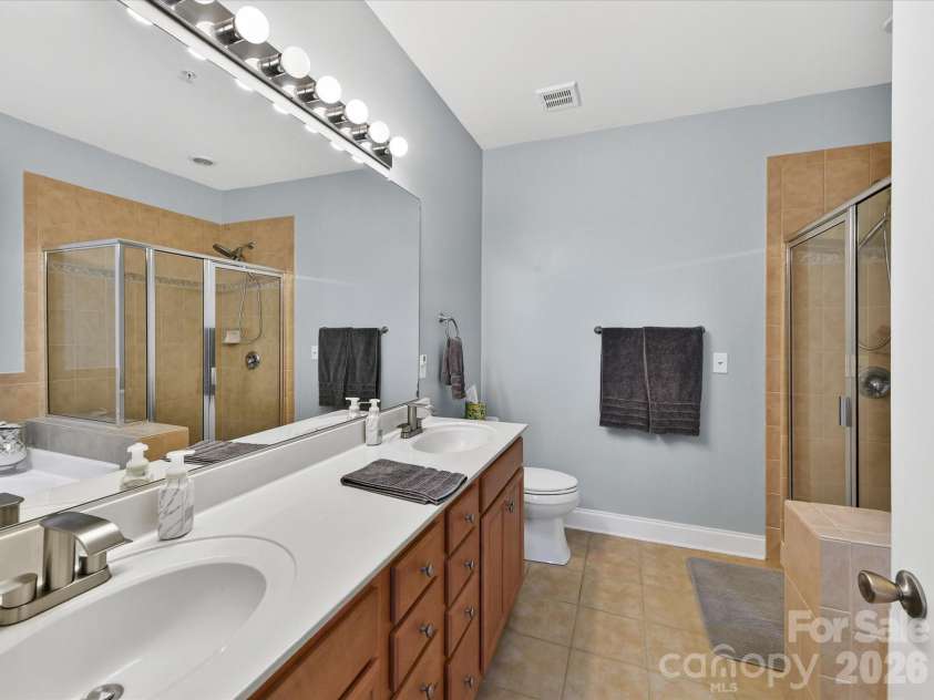 8665 Edinburgh Square Drive, Cornelius, NC 28031.  MLS# CAR4357240, YatesRealty ID 15038. Spacious primary bath featuring a double vanity, large mirror, and separate glass-enclosed shower for a comfortable and functional layout.