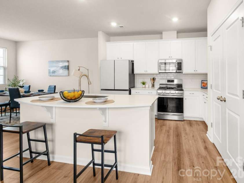 5044 Moss Pine Way, Tega Cay, SC 29708.  MLS# CAR4371971, YatesRealty ID 15096. The heart of the home. Quartz island with seating anchors this stunning open kitchen featuring stainless appliances, white shaker cabinets, subway tile backsplash, and a gas range — all overlooking the dining area.