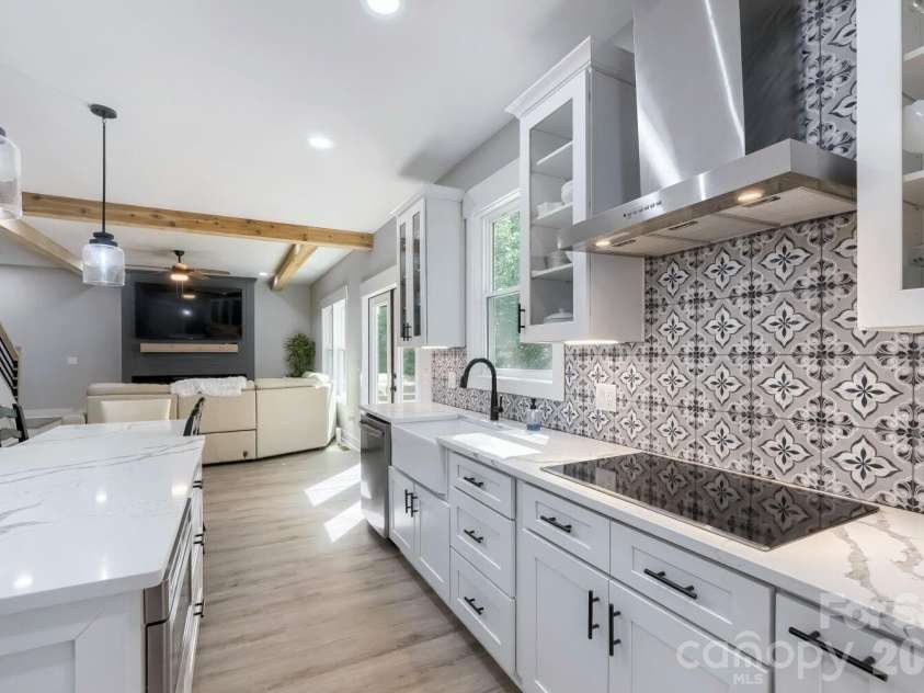 28838 Hwy 73 Highway, Albemarle, NC 28001.  MLS# CAR4373595, YatesRealty ID 15144. From the island looking toward the cook zone, this angle showcases the statement encaustic tile backsplash, stainless wall-mount range hood, farmhouse sink, black cooktop, and the seamless open sightline into the grea