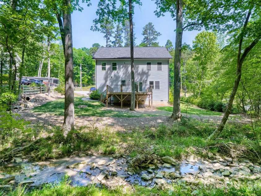 28838 Hwy 73 Highway, Albemarle, NC 28001.  MLS# CAR4373595, YatesRealty ID 15144. Rear elevation showcasing the elevated deck with cable railing, surrounded by mature hardwoods and a natural creek running along the back of the property.