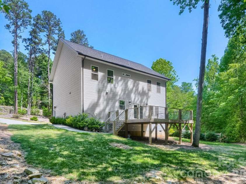 28838 Hwy 73 Highway, Albemarle, NC 28001.  MLS# CAR4373595, YatesRealty ID 15144. Side/rear view highlighting the elevated deck, cable rail staircase, lush green lawn, and wooded privacy that frames this serene outdoor setting.