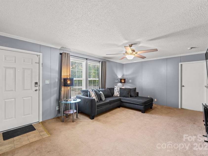 5039 Pine Springs Drive, Bessemer City, NC 28016.  MLS# CAR4249727, YatesRealty ID 15175. View from the eat in dining area into the living room.  The door to the left is the front door and the door to the right is the primary bedroom.  Large windows look out to the front yard and driveway