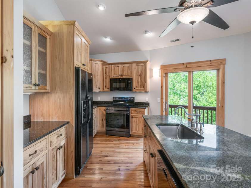 15 Sassy Lane, Asheville, NC 28805.  MLS# CAR4248835, YatesRealty ID 16032. Open kitchen with large island sink, under-cabinet lighting, and dark appliances. Kitchen overlooks 5 sets of glass sliding doors with long range mountain views