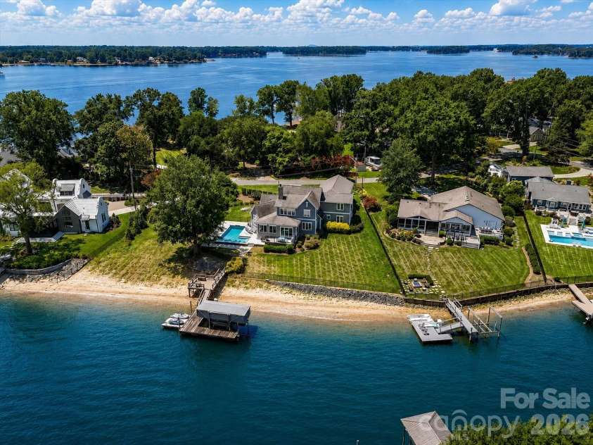 18014 Whispering Oaks Drive, Cornelius, NC 28031.  MLS# CAR4356897, YatesRealty ID 16097. Aerial view showcases the property's private sandy beach, dock, pool, and exceptional waterfront setting with expansive Lake Norman views. (Virtually enhanced lake levels)