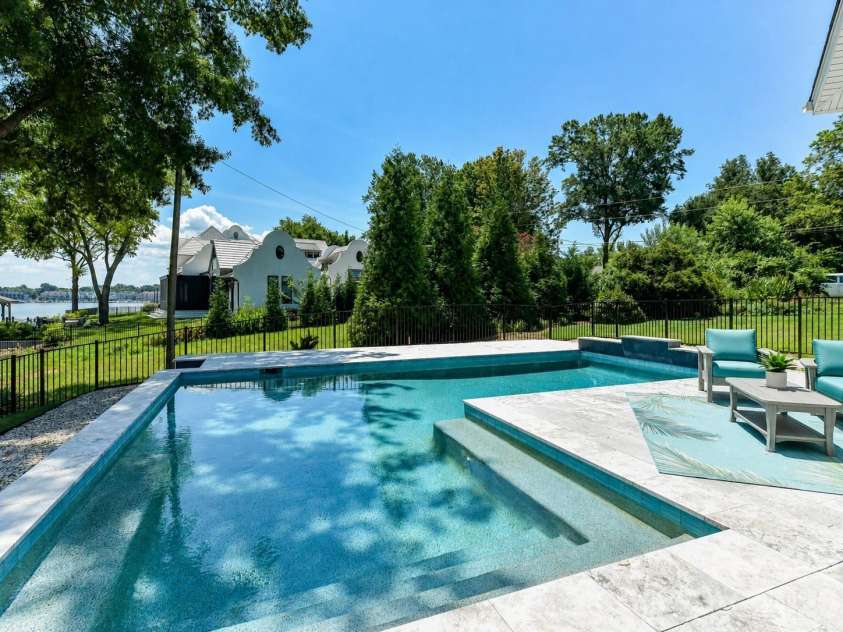 18014 Whispering Oaks Drive, Cornelius, NC 28031.  MLS# CAR4356897, YatesRealty ID 16097. Resort-style saltwater pool with expansive travertine decking creates a stunning outdoor retreat overlooking serene waterfront views, perfect for relaxing and entertaining.