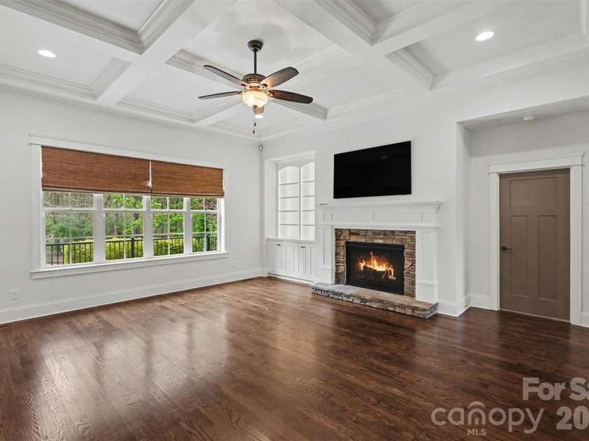 17909 Nodghia Circle, Davidson, NC 28036.  MLS# CAR4363596, YatesRealty ID 16766. Spacious Great Room featuring a charming fireplace and elegantly illuminated shelving units. The room is further enhanced by a beautifully detailed coffered ceiling, adding a touch of sophistication and architectural i