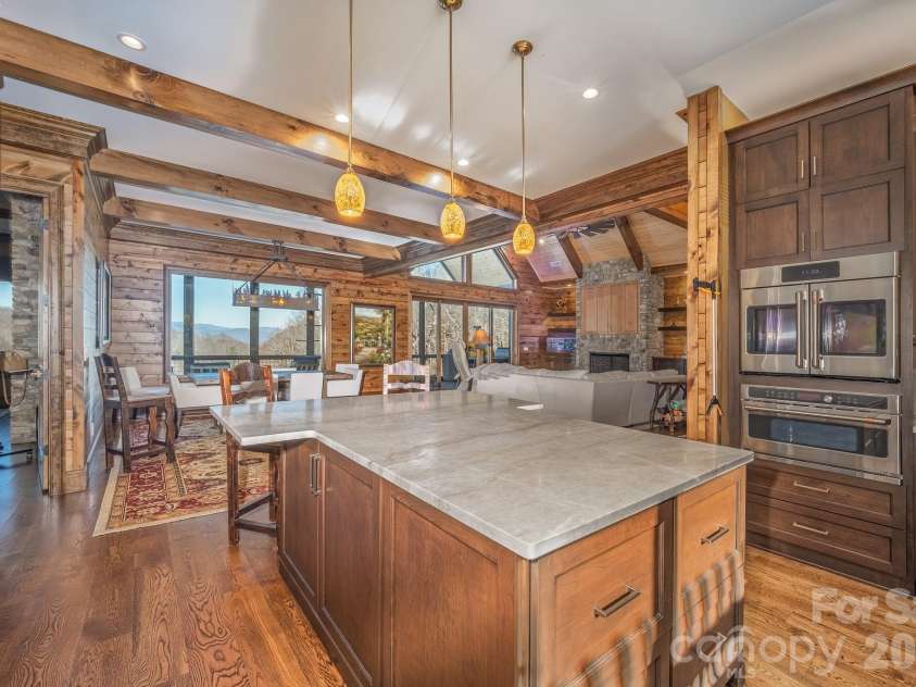 333 Kanasdatsi Drive, Brevard, NC 28712.  MLS# CAR4330137, YatesRealty ID 16902. Chef’s kitchen featuring a large center island with quartzite countertop, hand built wood cabinetry, wall ovens, exposed wood beams, and pendant lighting, opening seamlessly to the dining area and great room with mounta