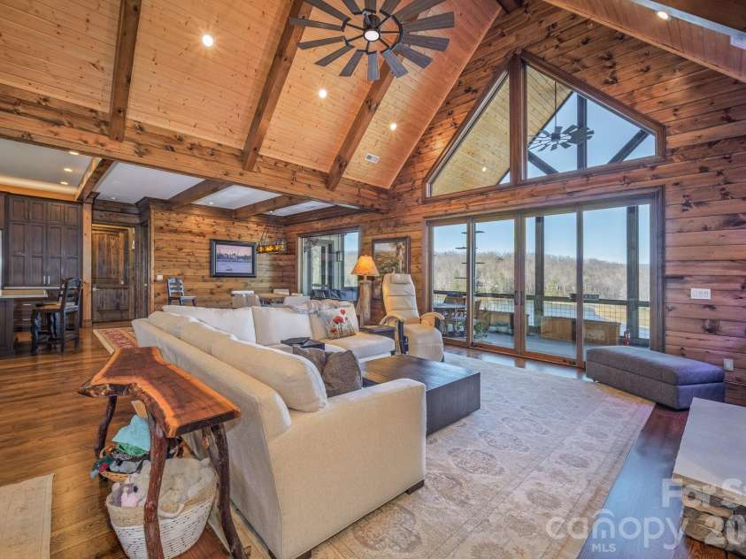 333 Kanasdatsi Drive, Brevard, NC 28712.  MLS# CAR4330137, YatesRealty ID 16902. Dramatic great room featuring soaring vaulted wood ceilings with exposed beams, expansive floor-to-ceiling windows, stone fireplace, and open-concept living that flows seamlessly to the covered deck with tranquil lake a