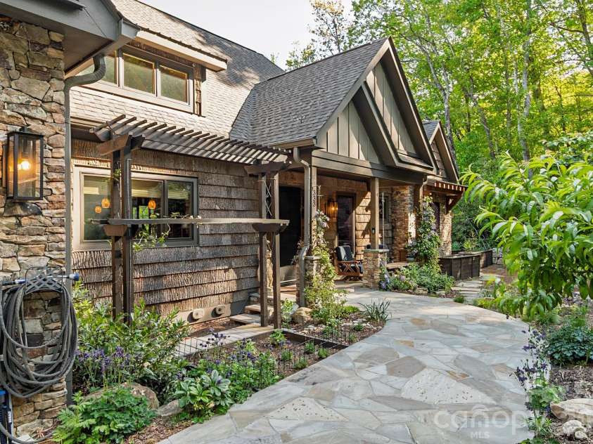 333 Kanasdatsi Drive, Brevard, NC 28712.  MLS# CAR4330137, YatesRealty ID 16902. Front exterior showcasing custom stone and wood craftsmanship, architectural rooflines, and a welcoming entry framed by landscaped pathways and natural surroundings.