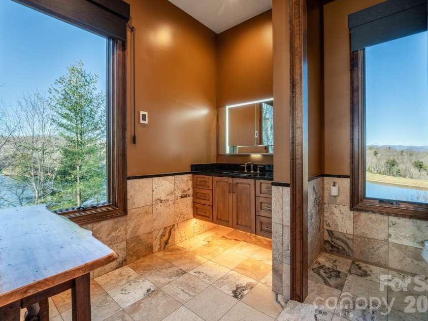 333 Kanasdatsi Drive, Brevard, NC 28712.  MLS# CAR4330137, YatesRealty ID 16902. Spa-inspired primary bathroom with stone tile flooring, dual vanity area, and private water closet, designed for comfort and elegance. (primary bath, stone tile, spa-like)