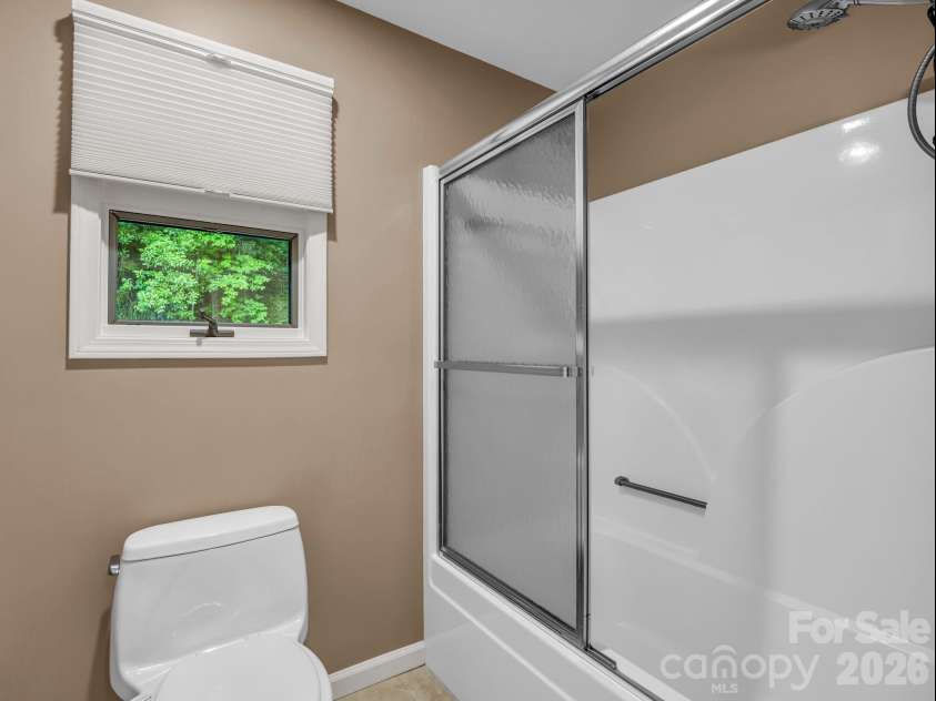 59 Agaliha Lane, Brevard, NC 28712.  MLS# CAR4392248, YatesRealty ID 1745. A bright, easy-access shower with sliding glass doors completes the comfortable primary bathroom setup.