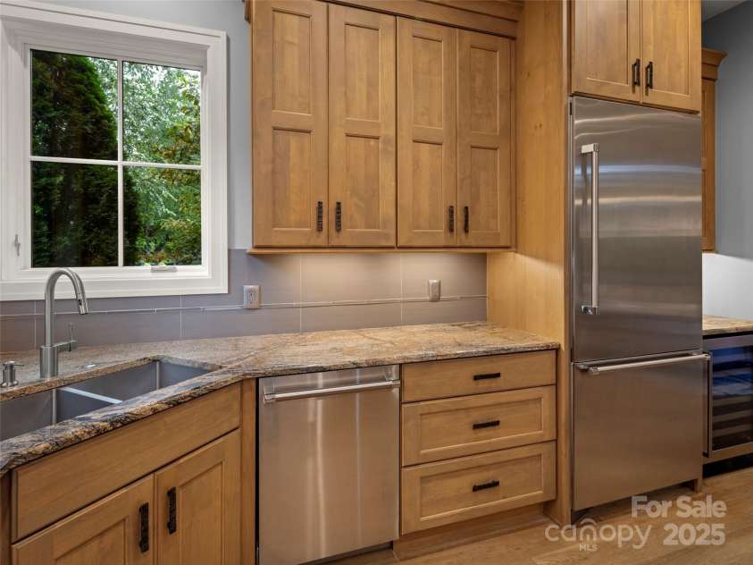 62 Running Creek Trail, Arden, NC 28704.  MLS# CAR4299725, YatesRealty ID 1785. Large double stainless sink under the corner windows. Thermador dishwasher, Thermador Refrigerator/Freezer and beverage cooler on the right. Ample custom cabinetry and drawers for storage. 