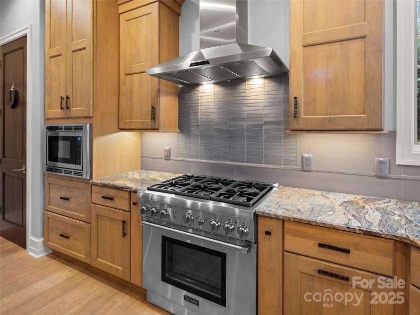 62 Running Creek Trail, Arden, NC 28704.  MLS# CAR4299725, YatesRealty ID 1785. Thermador natural gas six burner range with electric oven. Thermador exhaust hood. Thermador microwave.  Door on left is to large pantry with built-in shelving for efficient storage.  Glass tile backsplash provides a cle