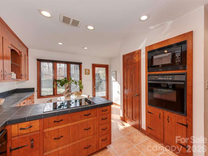 7244 Terrace Drive, Charlotte, NC 28211.  MLS# CAR4357695, YatesRealty ID 17887. Cooking in this warm, rustic, 1970s-inspired kitchen feels effortless. Enjoy rich wood cabinetry, beautiful dark tiled countertops, and a classic built-in oven and microwave wall, all bathed in abundant natural light. S