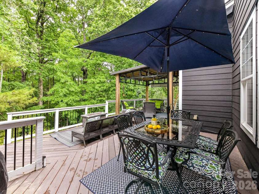 18721 The Commons Boulevard, Cornelius, NC 28031.  MLS# CAR4373232, YatesRealty ID 18371. Expansive open deck with multiple seating areas, dining space, and serene wooded views—perfect for entertaining or relaxing outdoors.