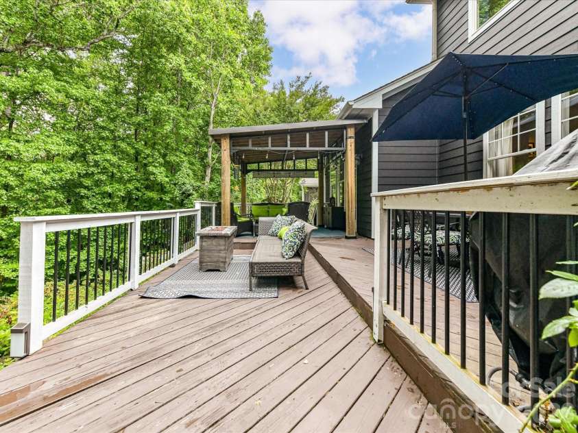 18721 The Commons Boulevard, Cornelius, NC 28031.  MLS# CAR4373232, YatesRealty ID 18371. Expansive open deck with multiple seating areas, dining space, and serene wooded views—perfect for entertaining or relaxing outdoors.