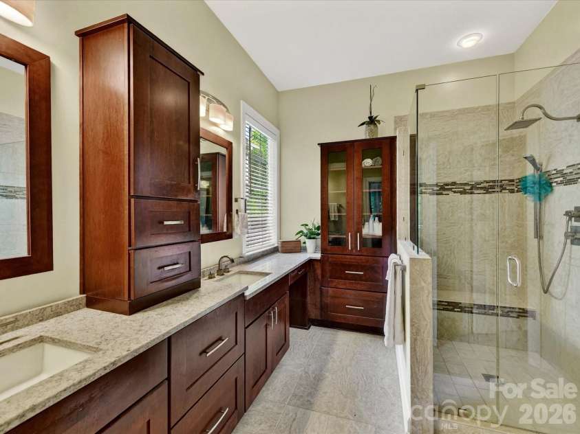 18721 The Commons Boulevard, Cornelius, NC 28031.  MLS# CAR4373232, YatesRealty ID 18371. Luxurious primary bath featuring dual vanities, granite countertops, and a spacious walk-in tiled shower with glass enclosure.