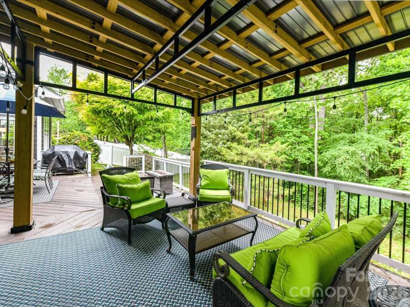 18721 The Commons Boulevard, Cornelius, NC 28031.  MLS# CAR4373232, YatesRealty ID 18371. Relax on the spacious covered deck featuring vaulted wood-beam ceilings, ambient string lighting, and peaceful wooded views—perfect for outdoor entertaining year-round.