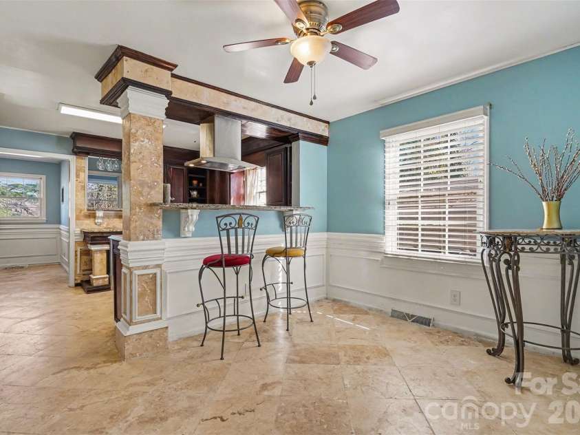 7144 CHAPPARALL Lane, Charlotte, NC 28215.  MLS# CAR4335752, YatesRealty ID 18633. Bright eat-in kitchen and breakfast area featuring travertine tile flooring, custom column accents, and bar-top seating overlooking the kitchen. Granite countertops, decorative corbels, and stainless vent hood add arc