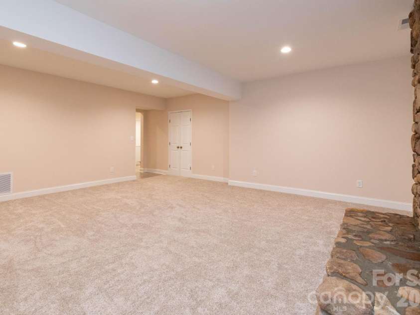 68 Sigmon Road, Fletcher, NC 28732.  MLS# CAR4336800, YatesRealty ID 18650. Additional view of the lower-level living space highlighting the rustic stone fireplace and generous open layout.
