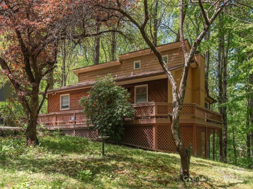 120 Blue Jay Loop, Maggie Valley, NC 28751.  MLS# CAR4242766, YatesRealty ID 18880. This cozy woodland cabin features a spacious wraparound deck nestled among mature trees, offering a peaceful retreat in a natural setting.