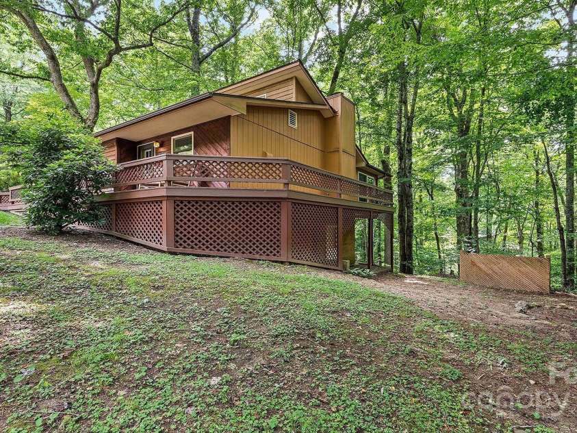 120 Blue Jay Loop, Maggie Valley, NC 28751.  MLS# CAR4242766, YatesRealty ID 18880. This cozy woodland cabin features a spacious wraparound deck nestled among mature trees, offering a peaceful retreat in a natural setting.
