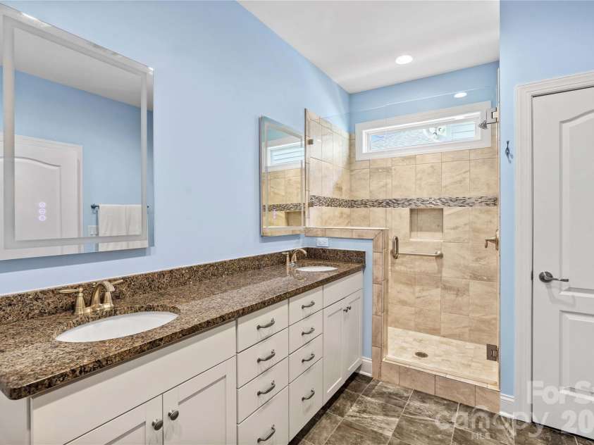 11528 Dublin Crescent Road, Cornelius, NC 28031.  MLS# CAR4364945, YatesRealty ID 19301. Primary bathroom with dual sinks, granite countertop, tiled shower with bench seating, tile floors, and spa-like mirrors which have different lighting options and defogging capabilities.