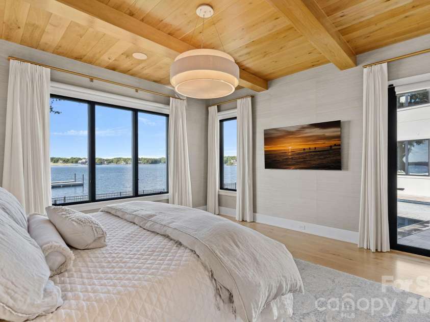 17811 Largo Place, Cornelius, NC 28031.  MLS# CAR4428601, YatesRealty ID 1945. Serene waterfront primary suite framed by sweeping lake views, a warm wood-plank ceiling with exposed beams and direct access to the pool terrace.