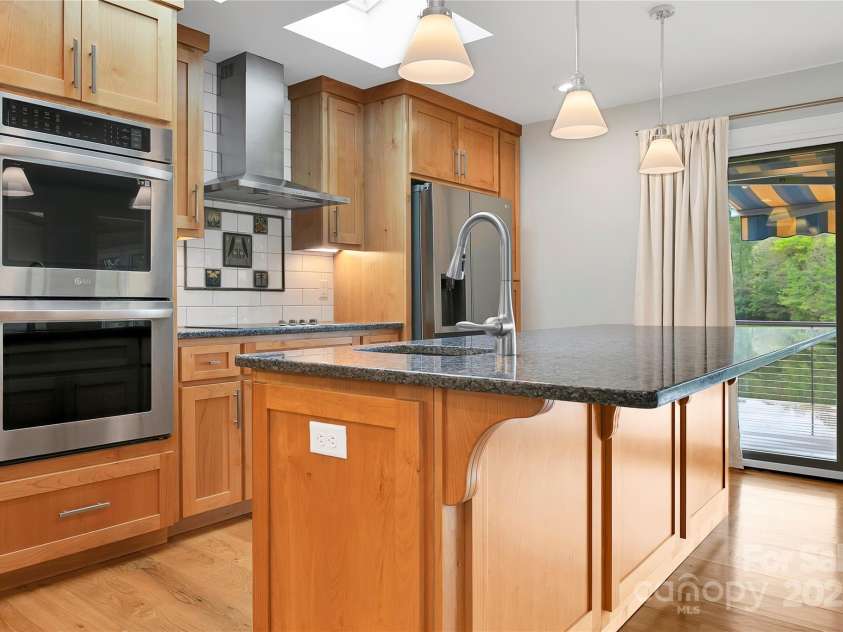 61 Tsataga Court, Brevard, NC 28712.  MLS# CAR4250347, YatesRealty ID 19462. Designed for both function and flair, this kitchen features double ovens, an induction cooktop with a vented hood, and a convenient bar sink. The well-planned work triangle makes cooking efficient and enjoyable.