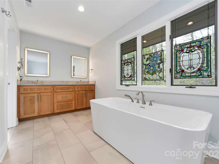 61 Tsataga Court, Brevard, NC 28712.  MLS# CAR4250347, YatesRealty ID 19462. The primary bathroom features a sleek double-sink vanity paired with modern fluorescent-lit mirrors.