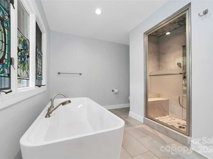 61 Tsataga Court, Brevard, NC 28712.  MLS# CAR4250347, YatesRealty ID 19462. Unwind in the luxurious primary bathroom, featuring a relaxing soaking tub and a rejuvenating steam shower—perfect after a day of hiking the scenic trails of Connestee Falls or enjoying a match of tennis, pickleball, or boc