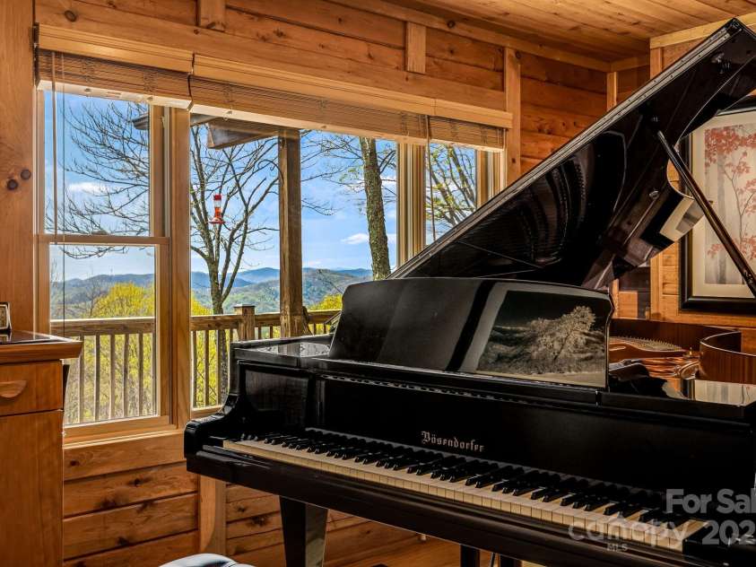 2399 El Miner Drive, Mars Hill, NC 28754.  MLS# CAR4259953, YatesRealty ID 19670. A stunning music room where a Bösendorfer grand piano stands proudly against a backdrop of sweeping mountain views, framed by warm wood tones and natural light.