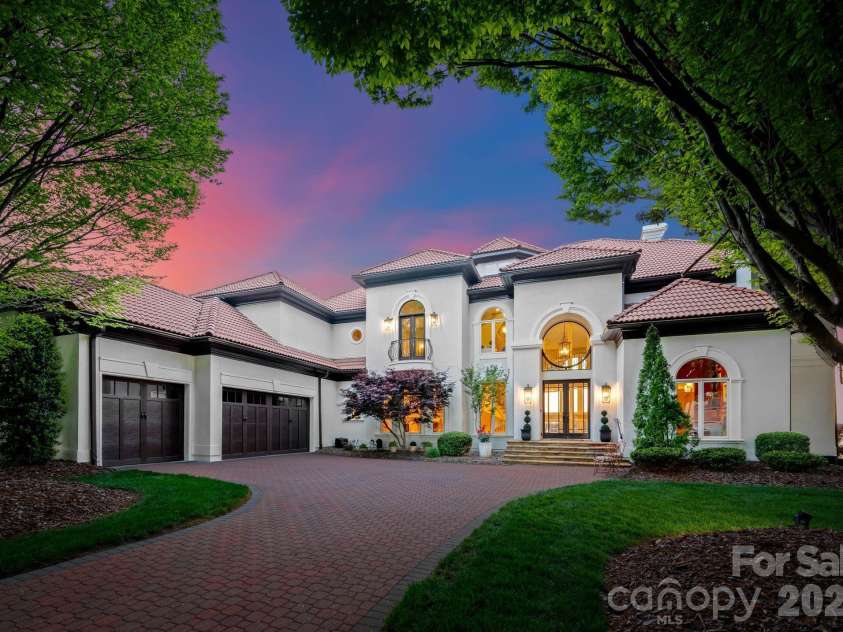 18103 Harbor Light Boulevard, Cornelius, NC 28031.  MLS# CAR4361515, YatesRealty ID 19890. Elegant front elevation at twilight, featuring a paver driveway, grand entry, and timeless Mediterranean-inspired design