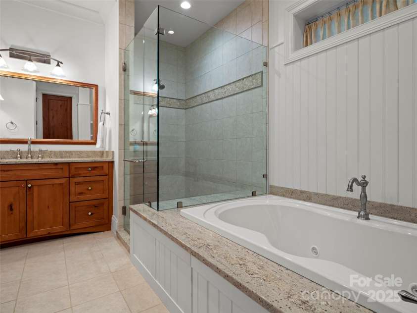 24 Deep Creek Trail, Arden, NC 28704.  MLS# CAR4264318, YatesRealty ID 20015. Terrace level second primary suite featurs double granite vanities, jetted tub with granite surround, frameless glass door shower and separate water closet, as well as a linen closet.