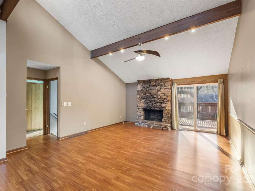 39 Oak Court, Fletcher, NC 28732.  MLS# CAR4330927, YatesRealty ID 20027. Living room with stone-framed gas logs fireplace, exposed wood beams, and access to deck.