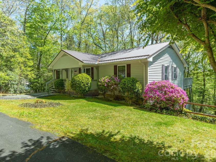 304 Emerald Hills Drive, Pisgah Forest, NC 28768.  MLS# CAR4373958, YatesRealty ID 20076. Front/Side Exterior – Side perspective highlights the home’s setting on a quiet, wooded lot with a spacious yard and blooming azaleas adding vibrant color.