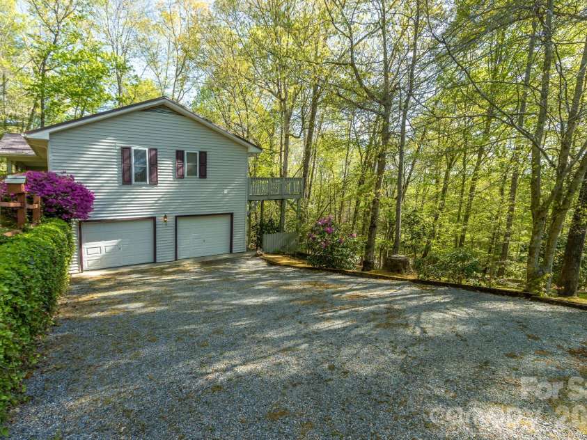 304 Emerald Hills Drive, Pisgah Forest, NC 28768.  MLS# CAR4373958, YatesRealty ID 20076. Side Exterior (Garage Level) – side view features a two-car garage with ample driveway space, set against a backdrop of mature trees for added privacy.