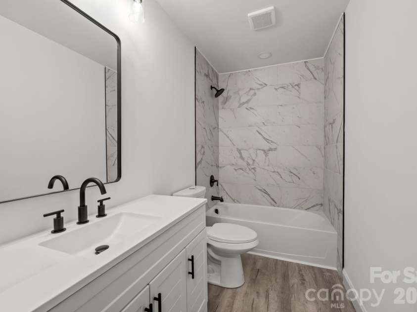 26 Poe Street, Rock Hill, SC 29730.  MLS# CAR4377637, YatesRealty ID 20117. This sleek second bathroom mirrors the home's designer finishes with a spacious tub and shower combination encased in floor-to-ceiling marble-style tile. The modern white vanity is elevated by a trendy matte black gooseneck 