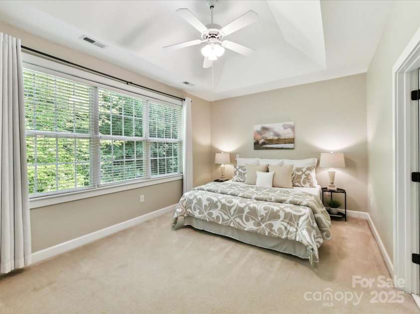 2215 Henery Tuckers Court, Charlotte, NC 28270.  MLS# CAR4267429, YatesRealty ID 20299. A spacious primary bedroom suite features a tray ceiling and is located on the main level and overlooks a wooded setting in the backyard